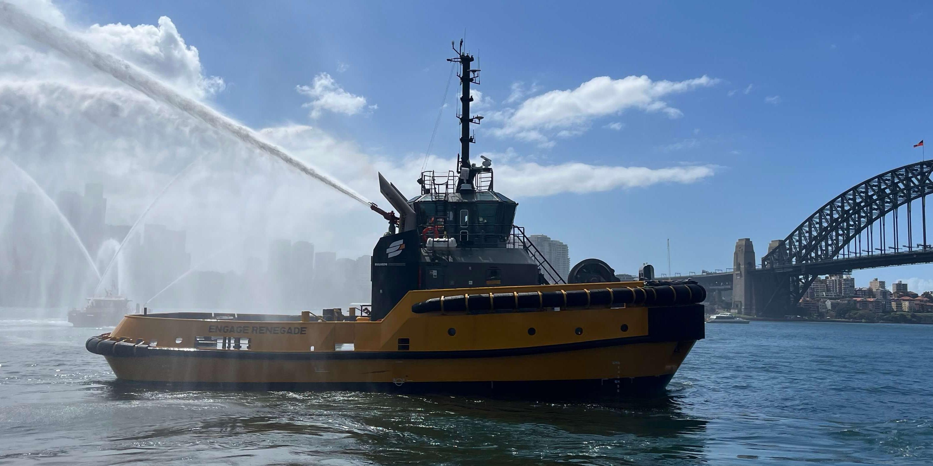 Engage Renegade, a DAMEN AD TUG 2813, spraying water in a ceremonial display against the backdrop of the Sydney Harbour Bridge, with a clear blue sky overhead.